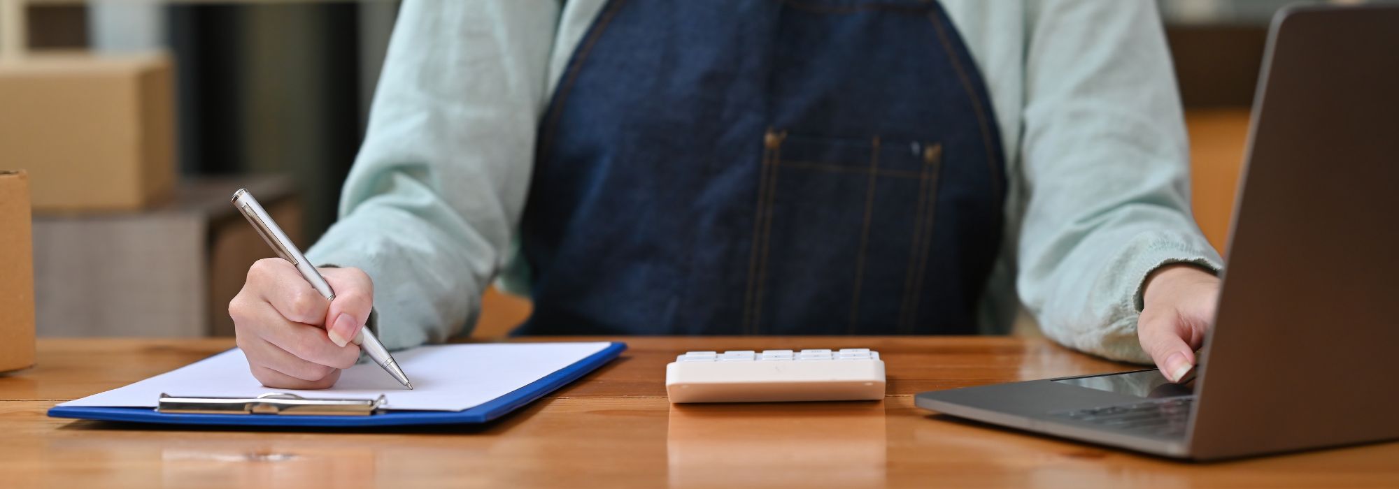 Photo of a business owner in an apron writing on a clipboard