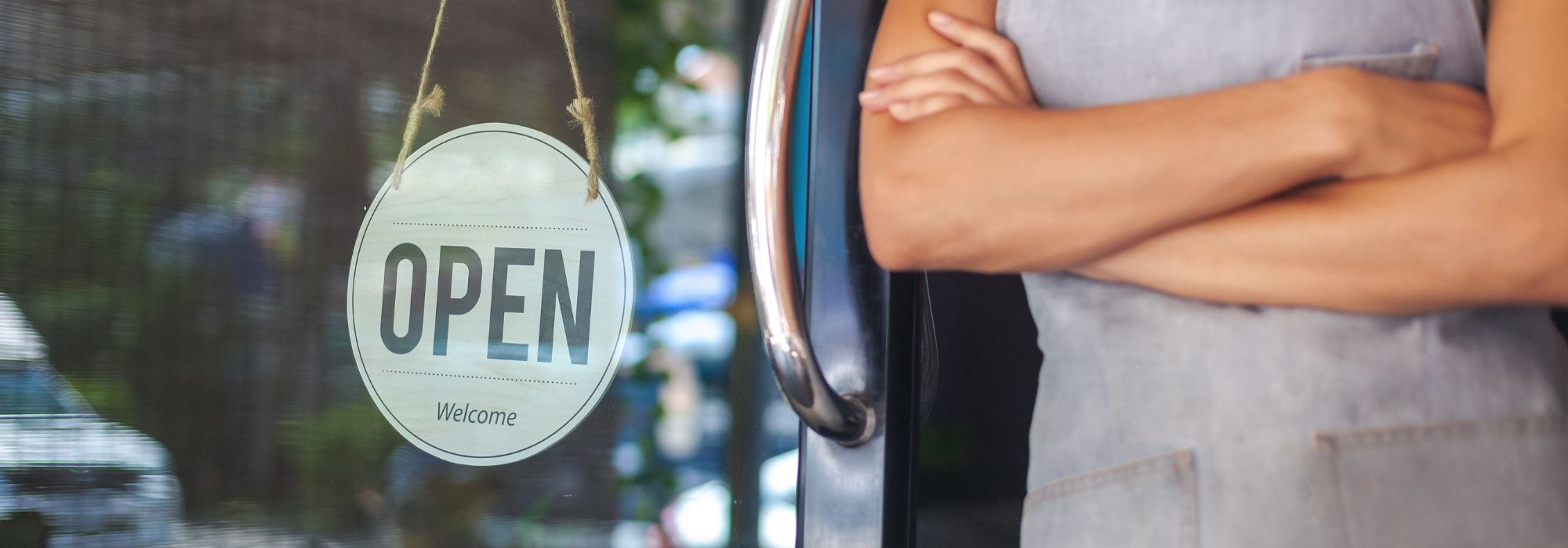 Small business owner standing in front of their store with an open sign