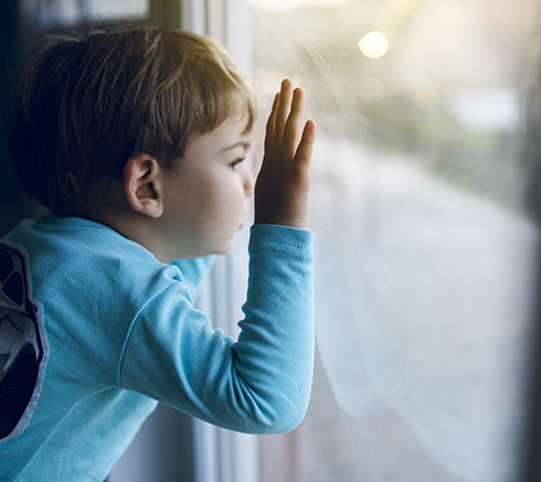 Little boy at home looking trough the window waiting for his mot