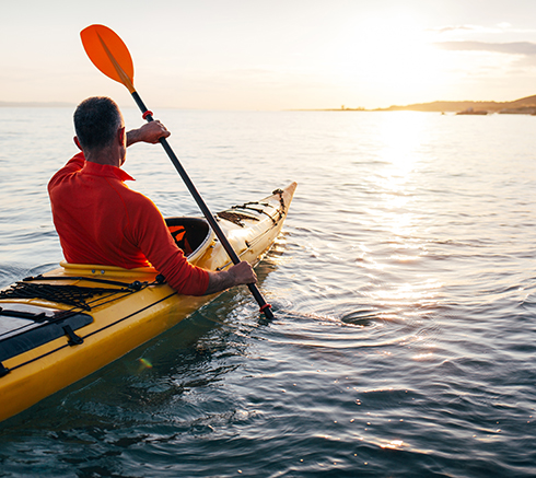 Senior man paddling kayak on the sunset sea