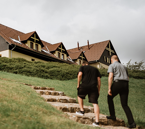 Grassy hill with big cottage on top. The cottage has wooden arca