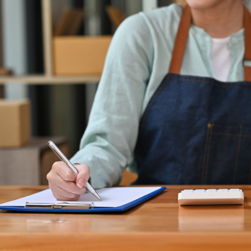 Photo of a business owner in an apron writing on a clipboard