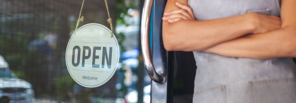 Small business owner standing in front of their store with an open sign