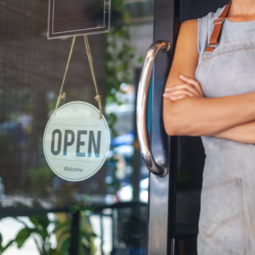 Small business owner standing in front of their store with an open sign