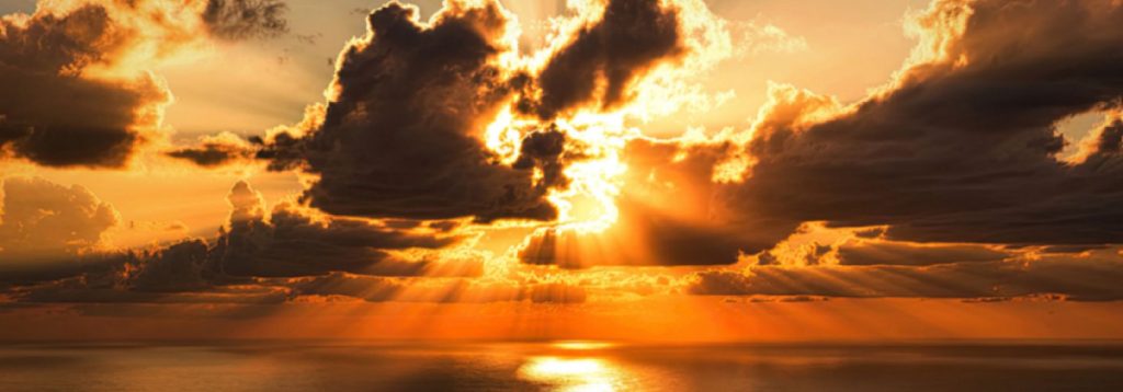 Photo of sun setting through the clouds over a body of water