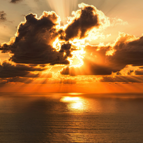 Photo of sun setting through the clouds over a body of water