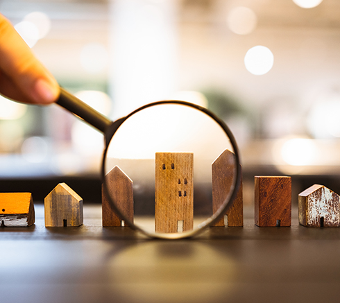 Hand holding magnifying glass and looking at house model, house